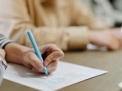 Zwei Personen füllen an einem Tisch Formulare aus, oben rechts ist das Logo „College für Osteop